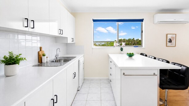 A modern kitchen with white cabinets, a stainless steel sink, and a window with a view of the outdoors. - Carlenes Getaway | Lake Views, Beach & Games Hub (Loch Sport)
