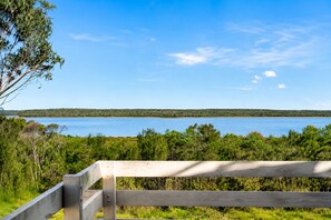 A wooden bench overlooking a body of water with a distant tree line. - Carlenes Getaway | Lake Views, Beach & Games Hub (Loch Sport)