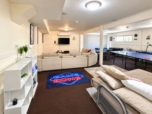 A modern living room with a sofa, a TV, and a ping pong table. - Carlenes Getaway | Lake Views, Beach & Games Hub (Loch Sport)