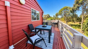 A red building with a deck, outdoor seating, and a view of trees. - Carlenes Getaway | Lake Views, Beach & Games Hub (Loch Sport)