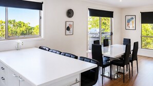 A modern kitchen with a white countertop, black chairs, and a dining table. - Carlenes Getaway | Lake Views, Beach & Games Hub (Loch Sport)
