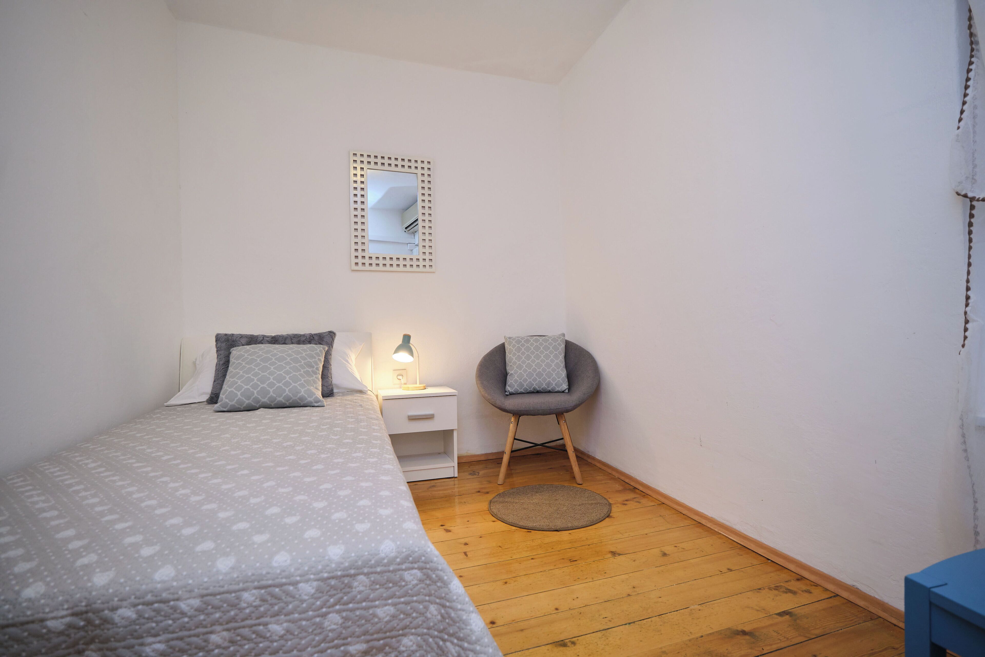 Une chambre à coucher comprenant un lit, une table de chevet, une chaise et un petit tapis rond.