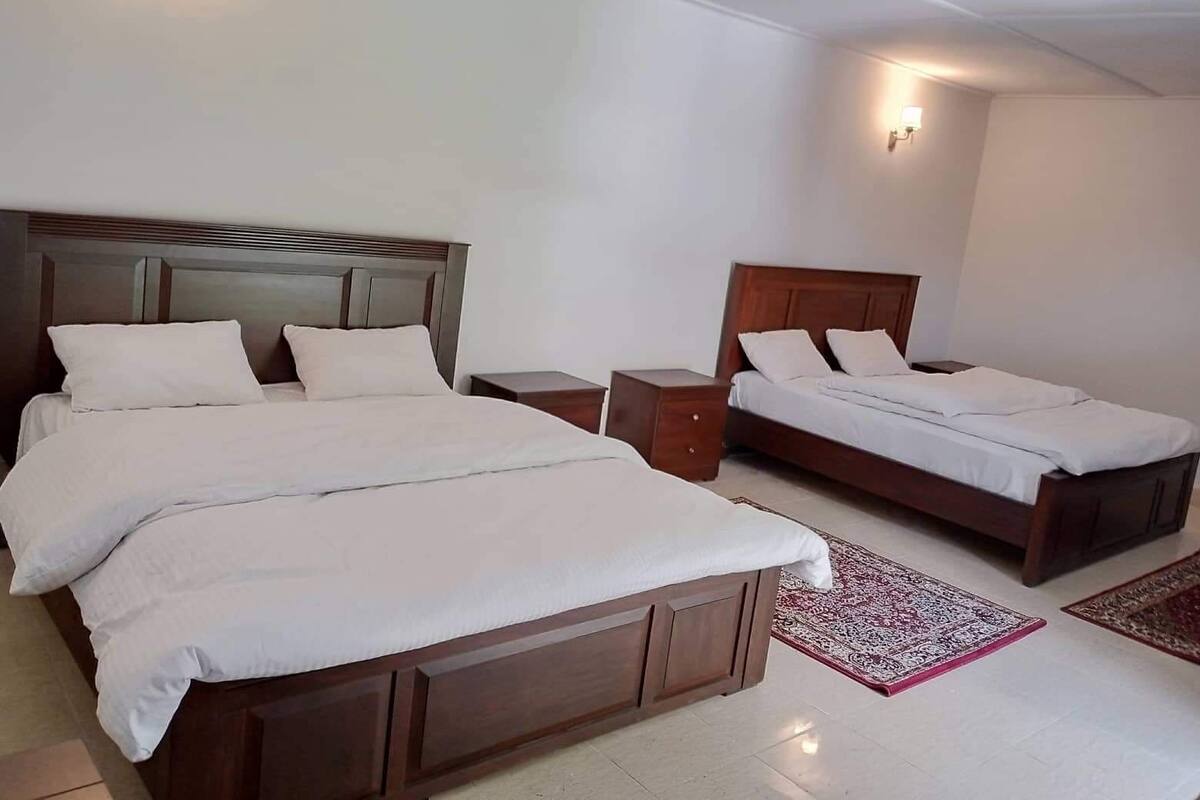 A hotel room with two beds, a nightstand, and a small table.