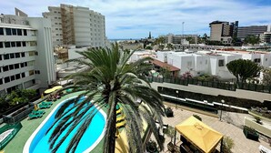 Un espace piscine aménagé sur le toit, avec des palmiers, un ciel dégagé et des bâtiments environnants.