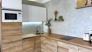 Una cocina moderna con microondas integrado, un lavabo, armarios de madera, una lámpara colgante y un estante pequeño con adornos.