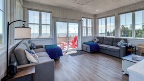 Una habitación amplia con ventanas grandes, techo de madera y un rincón de descanso acogedor con un sofá y sillones.