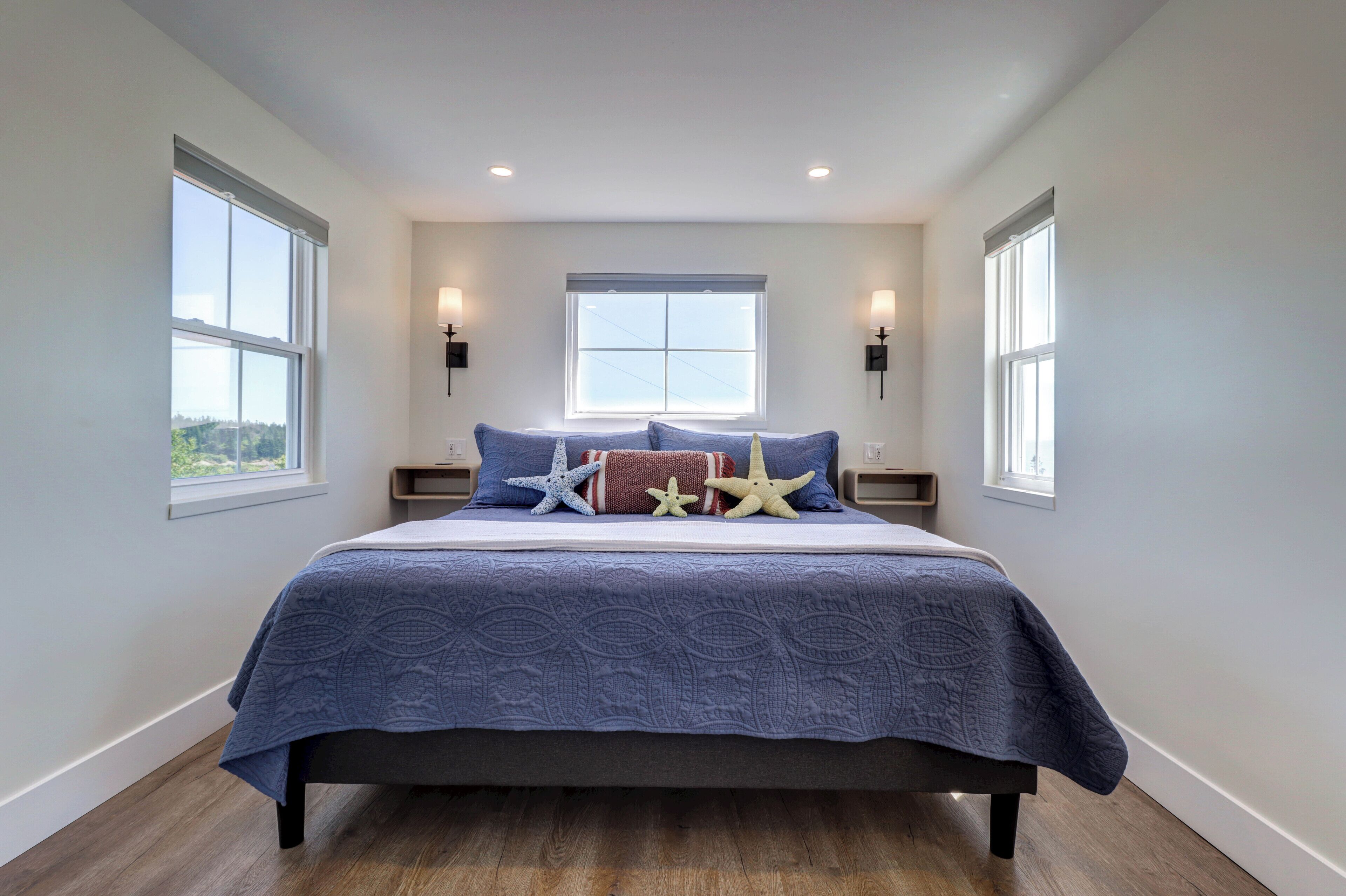 A bedroom with a large bed, two bedside tables, a window, and wall-mounted lights.