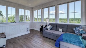 Una habitación amplia con ventanas grandes, un sofá gris y suelo de madera.
