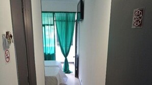 Een smalle gang die leidt naar een slaapkamer met een bed, een aan de muur bevestigde televisie en een deur met een nummerbord.