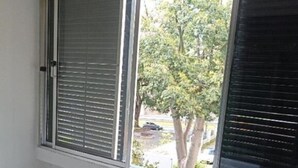 Een kamer met een groot raam, witte wanden en een houten vloer.