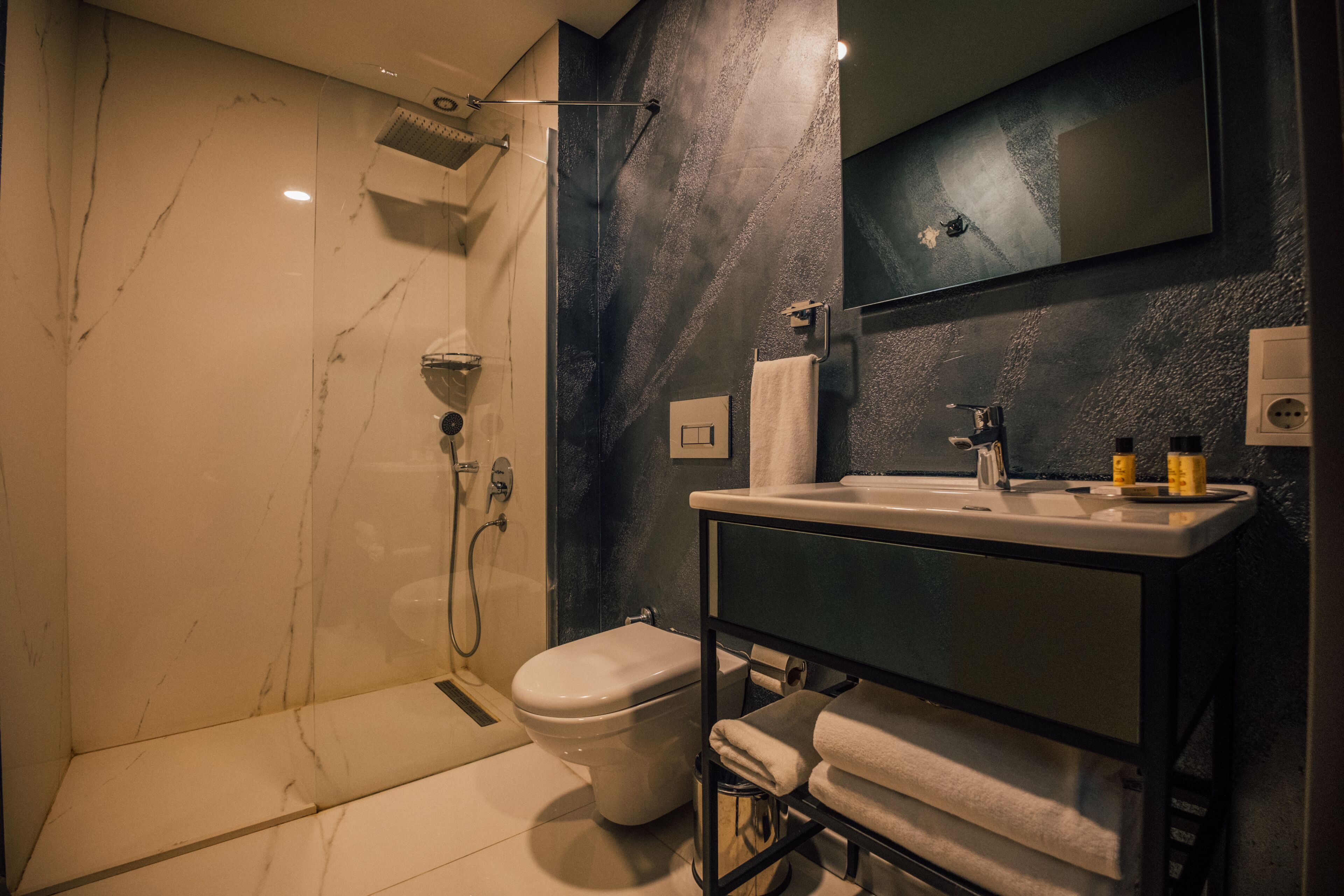 A modern bathroom with a marble shower, a toilet, a sink with a mirror, and a towel rack.