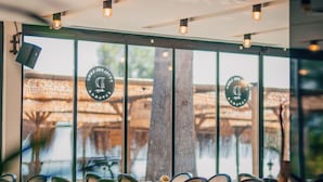 L’intérieur d’un restaurant, avec des tables et des chaises, de grandes fenêtres et un arbre visible à l’extérieur.
