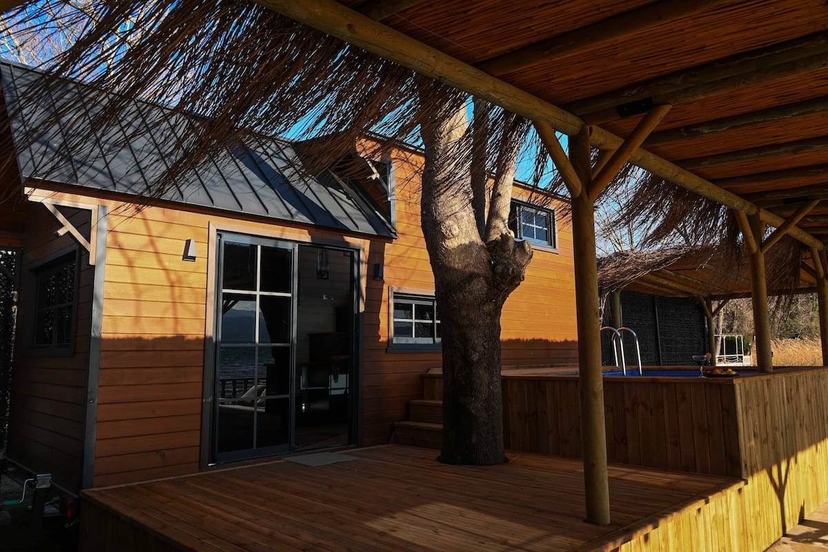 A wooden deck with a covered area, a large tree, and a house with a glass door and windows.
