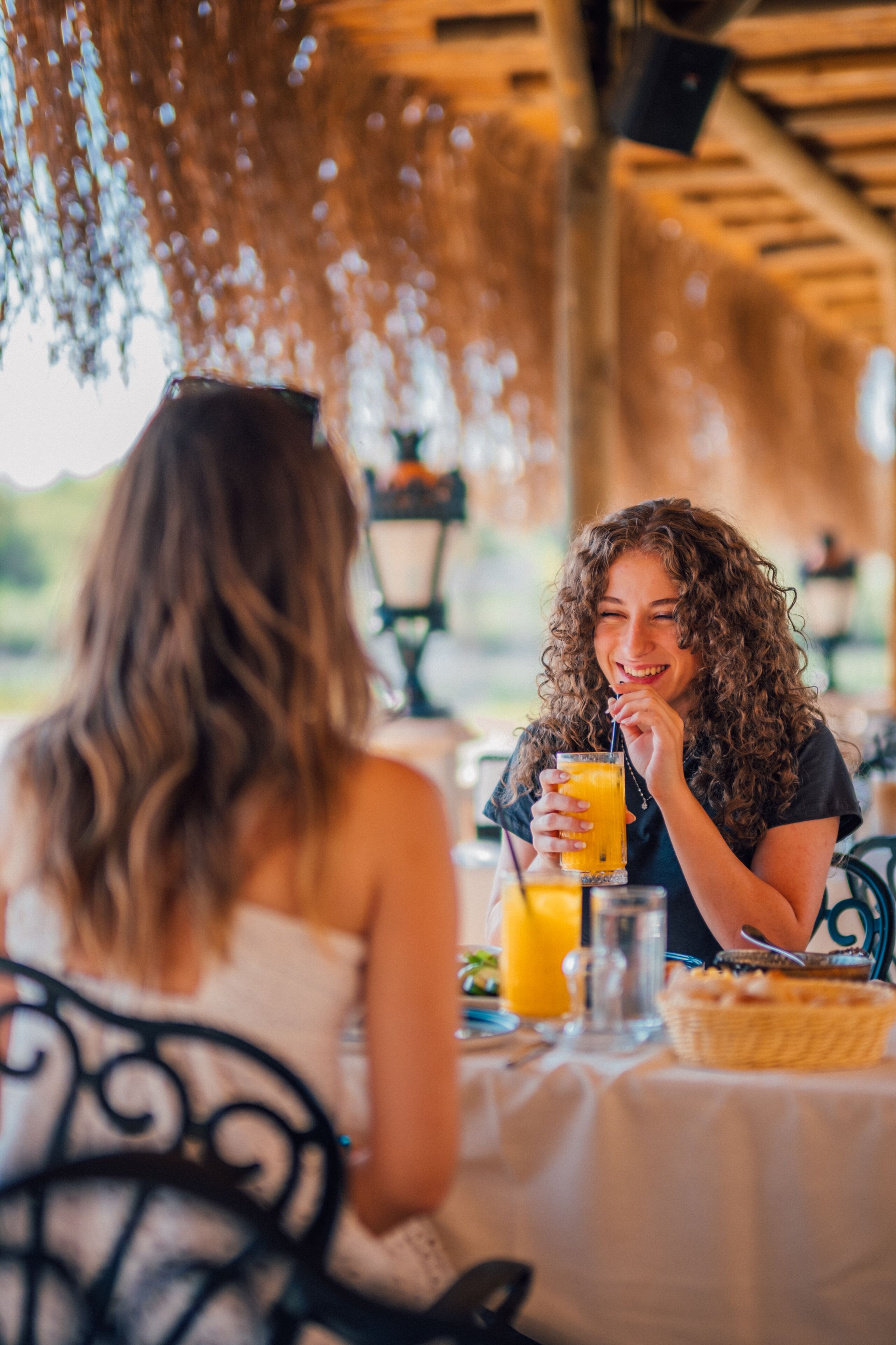 A person sitting at a table with a drink, under a canopy with hanging decorations.