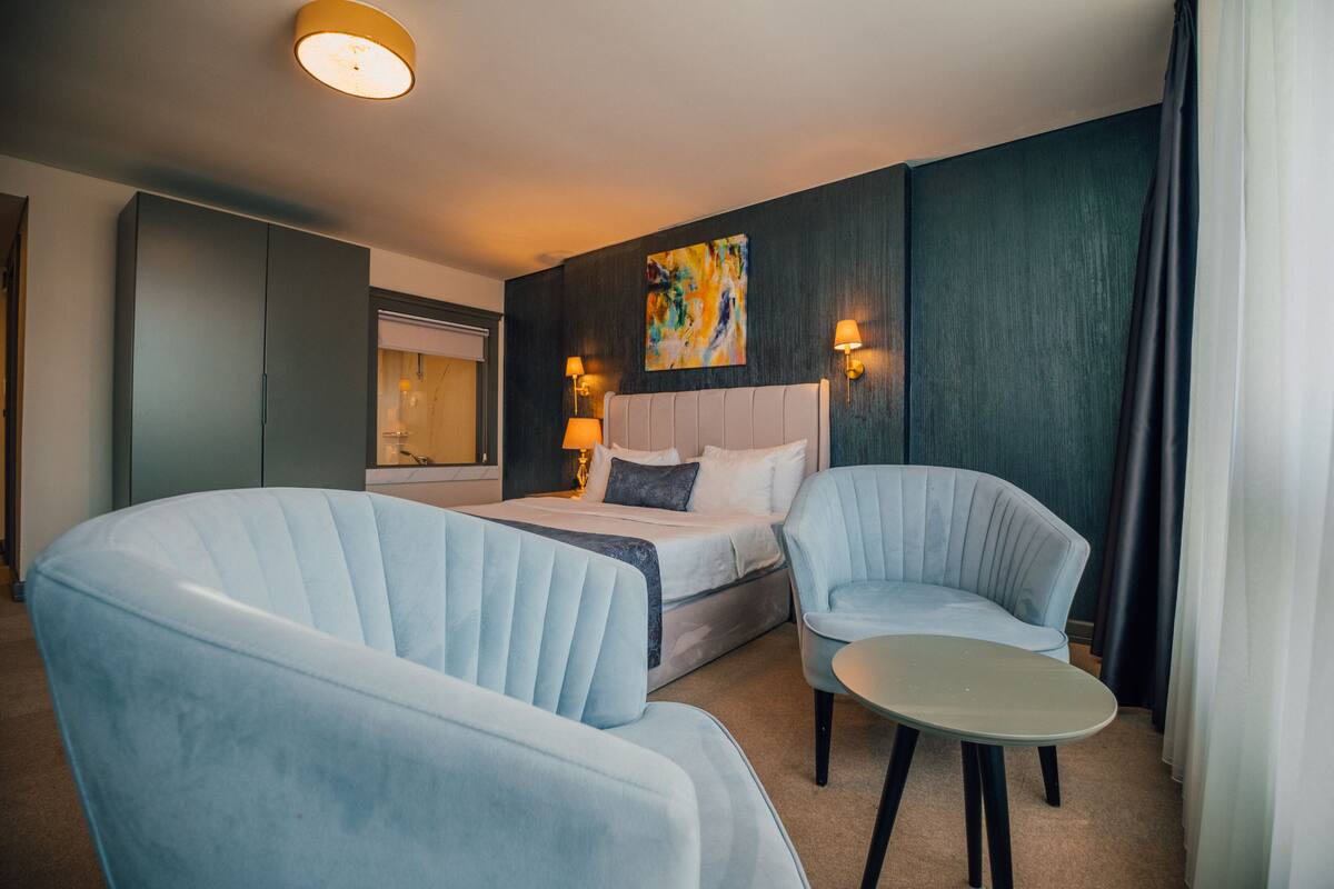 A hotel room with a bed, two armchairs, a small table, and a painting on the wall.