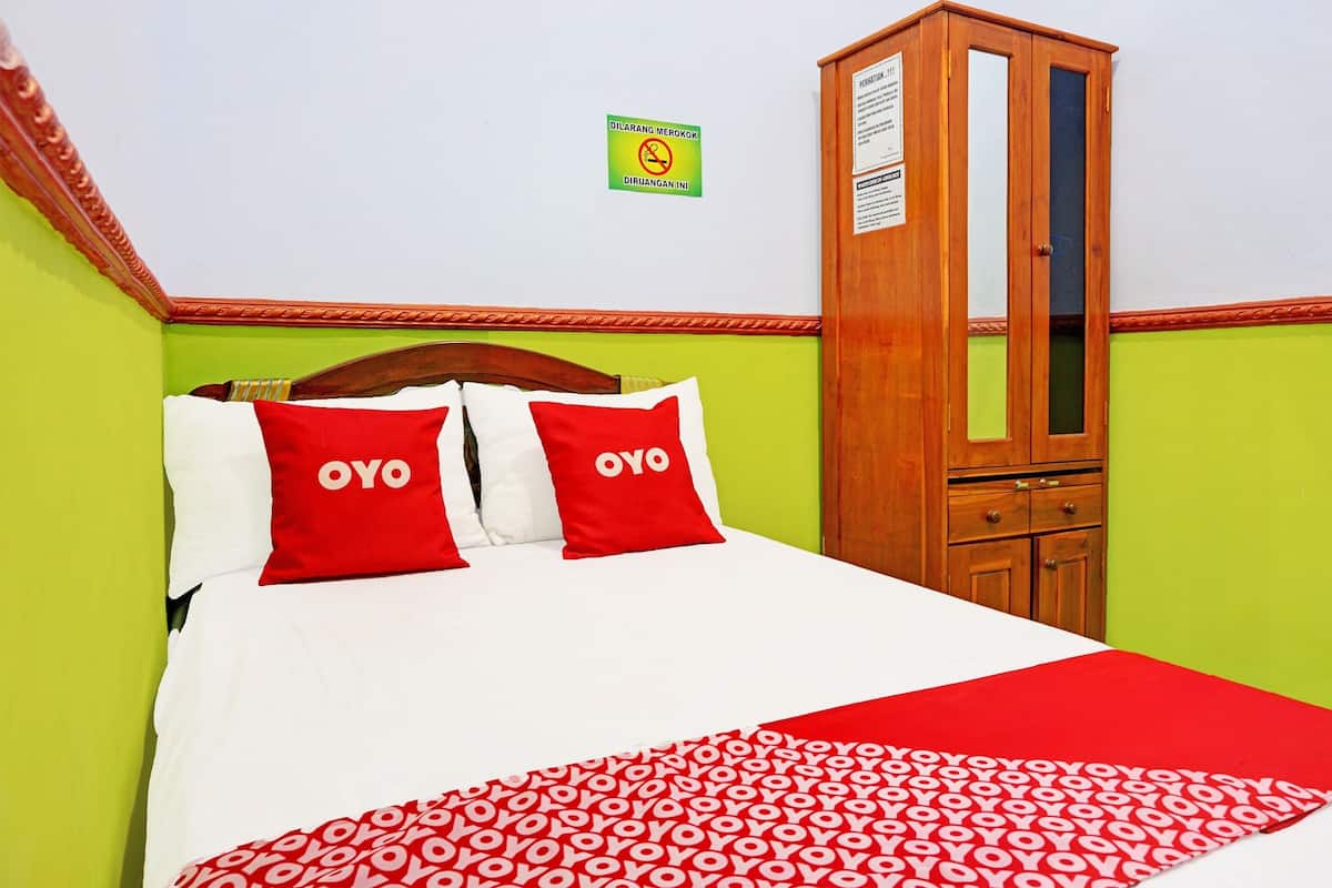 Un lit avec une literie rouge et blanche, une armoire en bois et un panneau accroché au mur.
