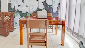 A wooden dining table with chairs, a laptop on the table, and a floral wallpaper in the background.