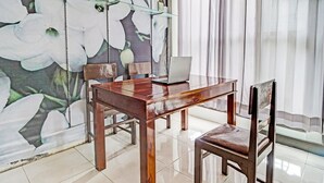 A wooden table with a laptop, two chairs, and a glass partition in a room with a tiled floor and a floral mural on the wall.