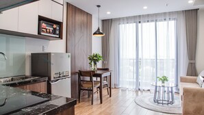 Une cuisine moderne équipée d’un four encastré, d’un réfrigérateur et d’un four à micro-ondes posé sur le plan de travail. On y trouve également un coin repas avec une table et des chaises, ainsi qu’un canapé dans le salon.