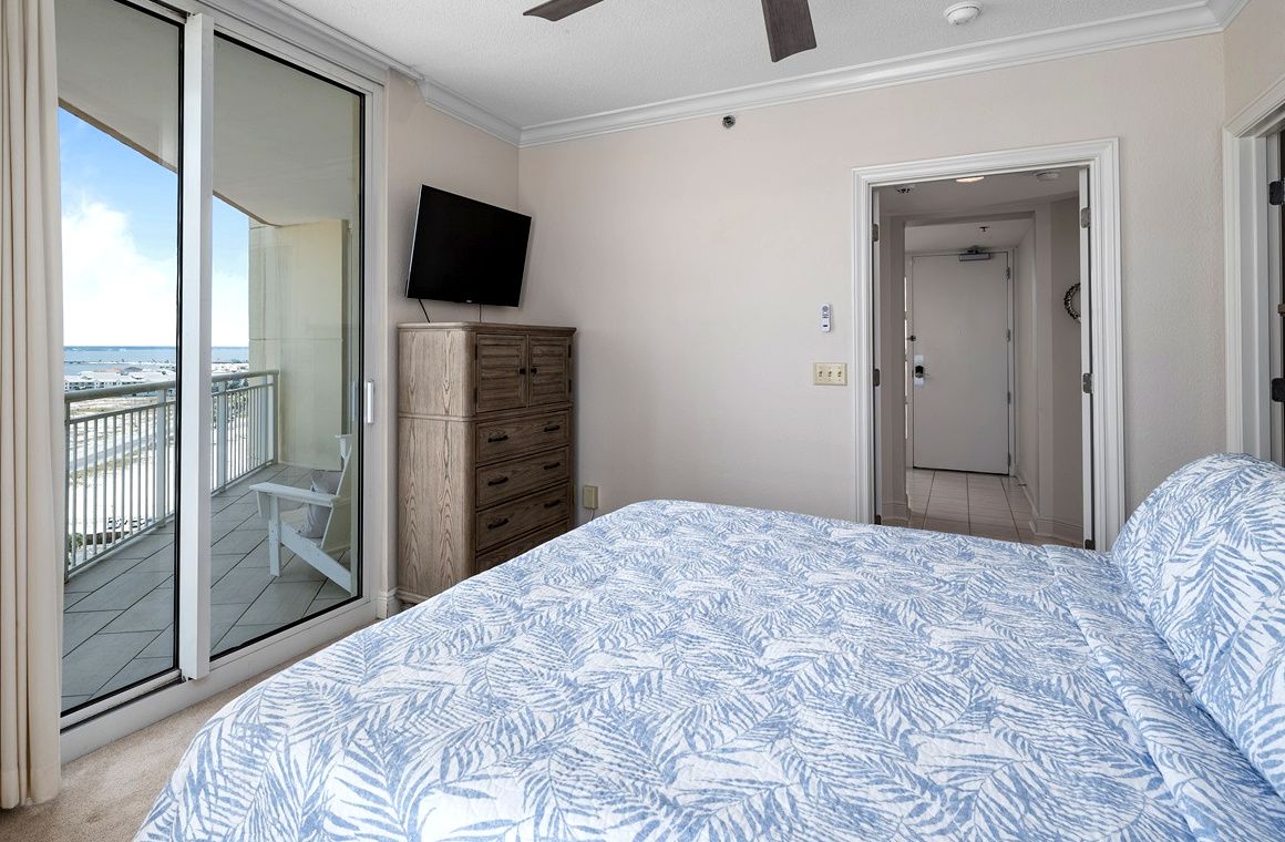 Ein Schlafzimmer mit einem Bett, einem Fernseher, einem Kleiderschrank und einer Schiebetür zum Balkon.
