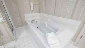 Une salle de bain moderne avec une grande baignoire, des carreaux blancs et un motif décoratif en forme de feuilles sur les murs.