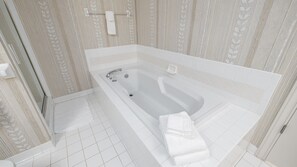 A modern bathroom with a large bathtub, white tiles, and a decorative leaf pattern on the walls. - Epic 4BR/4BA Gulf Front | Free Beach Chair Service (Navarre)