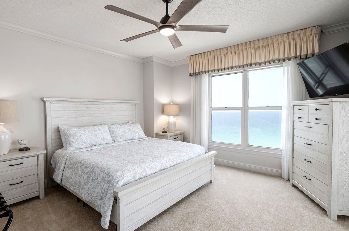 Un dormitorio con cama, mesitas de noche, lámpara, televisor, cómoda y ventana con vistas.