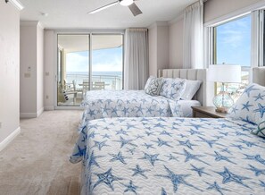 A hotel room with two beds, a balcony with a view, and a ceiling fan.
