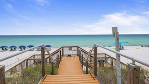 A wooden boardwalk leading to a beach with blue umbrellas and lounge chairs. - Epic 4BR/4BA Gulf Front | Free Beach Chair Service (Navarre)