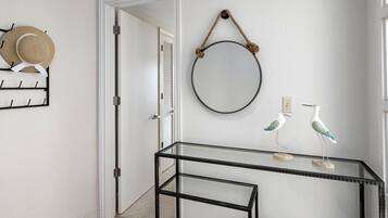 A hallway with a glass table, a round mirror, and decorative items including a hat rack and bird figurines.