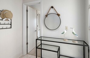 Un pasillo con una mesa de vidrio, un espejo redondo y elementos decorativos, incluyendo un perchero y figuritas de pájaros.