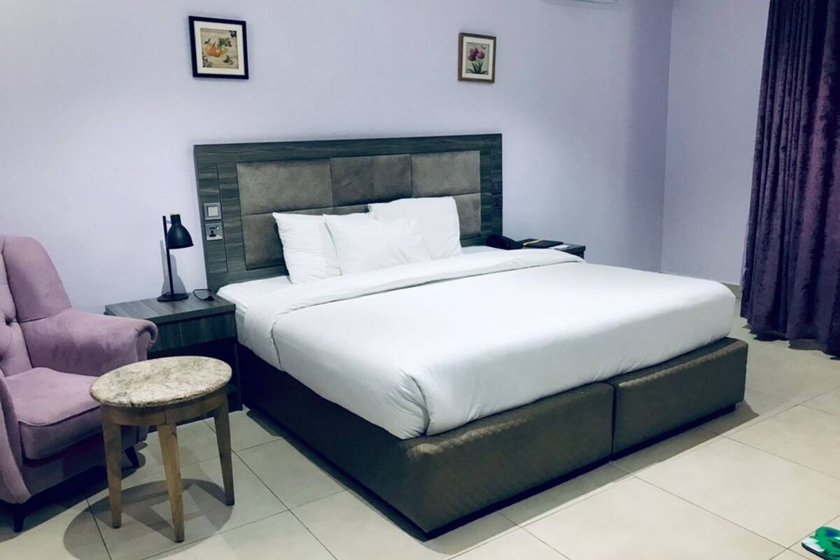 A hotel room with a large bed, a nightstand, a chair, and a small table.
