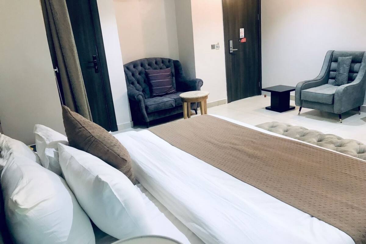 A hotel room with a bed, a sofa, a chair, and a small table.