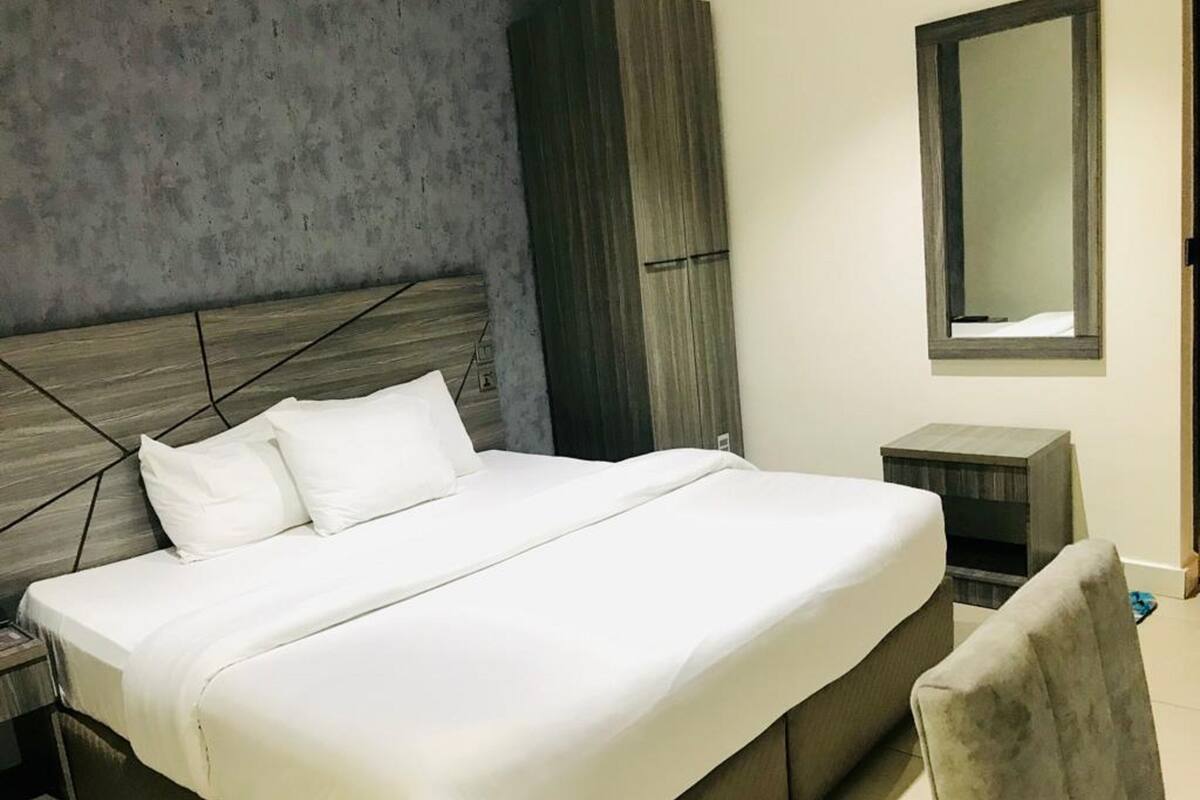 A modern bedroom with a large bed, a nightstand, a wardrobe, and a mirror on the wall.