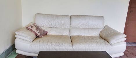 A white leather sofa with a patterned pillow against a plain wall, a black table in front, and a tiled floor.