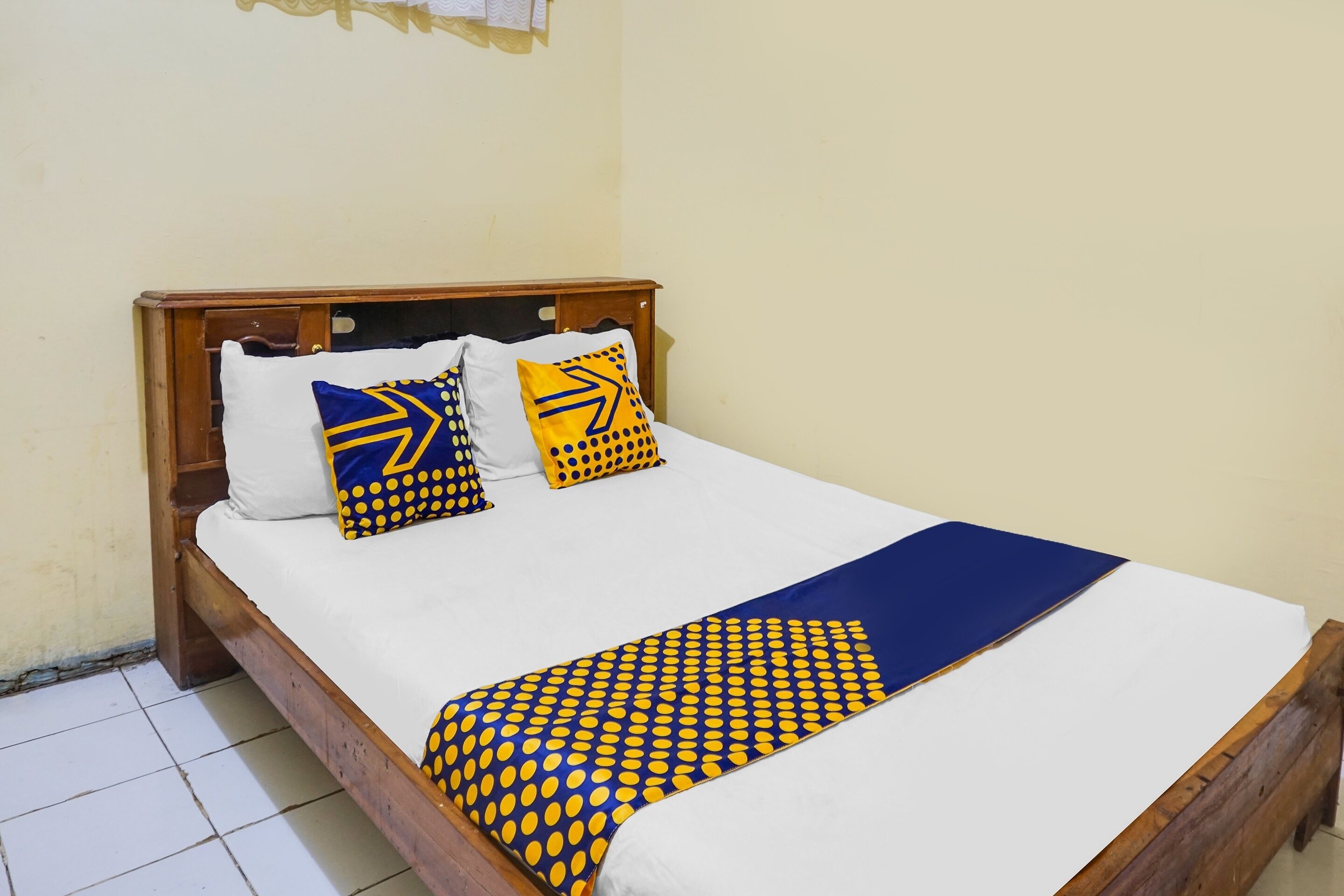 A bed with a wooden frame, white bedding, and patterned pillows.