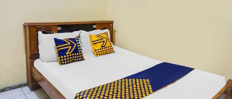 Un letto con struttura in legno, biancheria bianca e cuscini decorati.