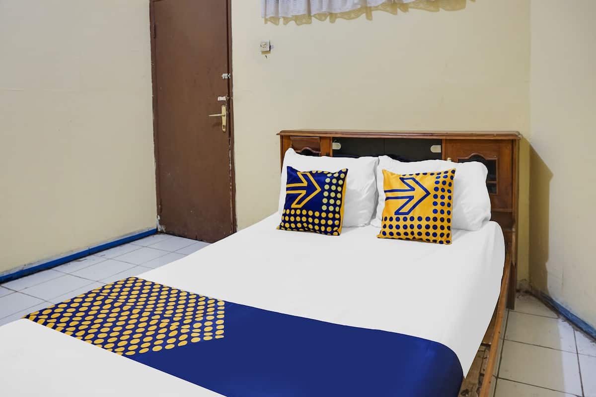 A neatly made bed with a blue and yellow patterned bedspread and pillows, a wooden headboard, and a white wall with a door to the left.