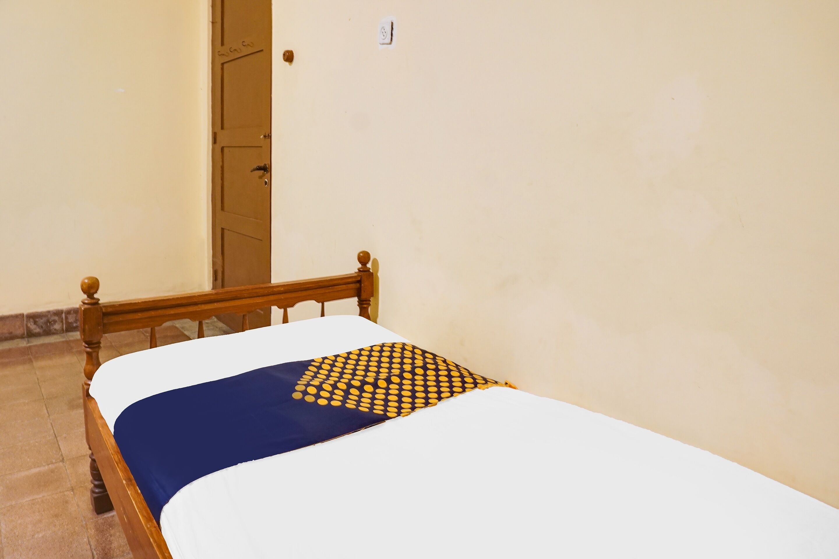 A single bed with a white mattress and a blue blanket, a wooden headboard, and a patterned pillow.