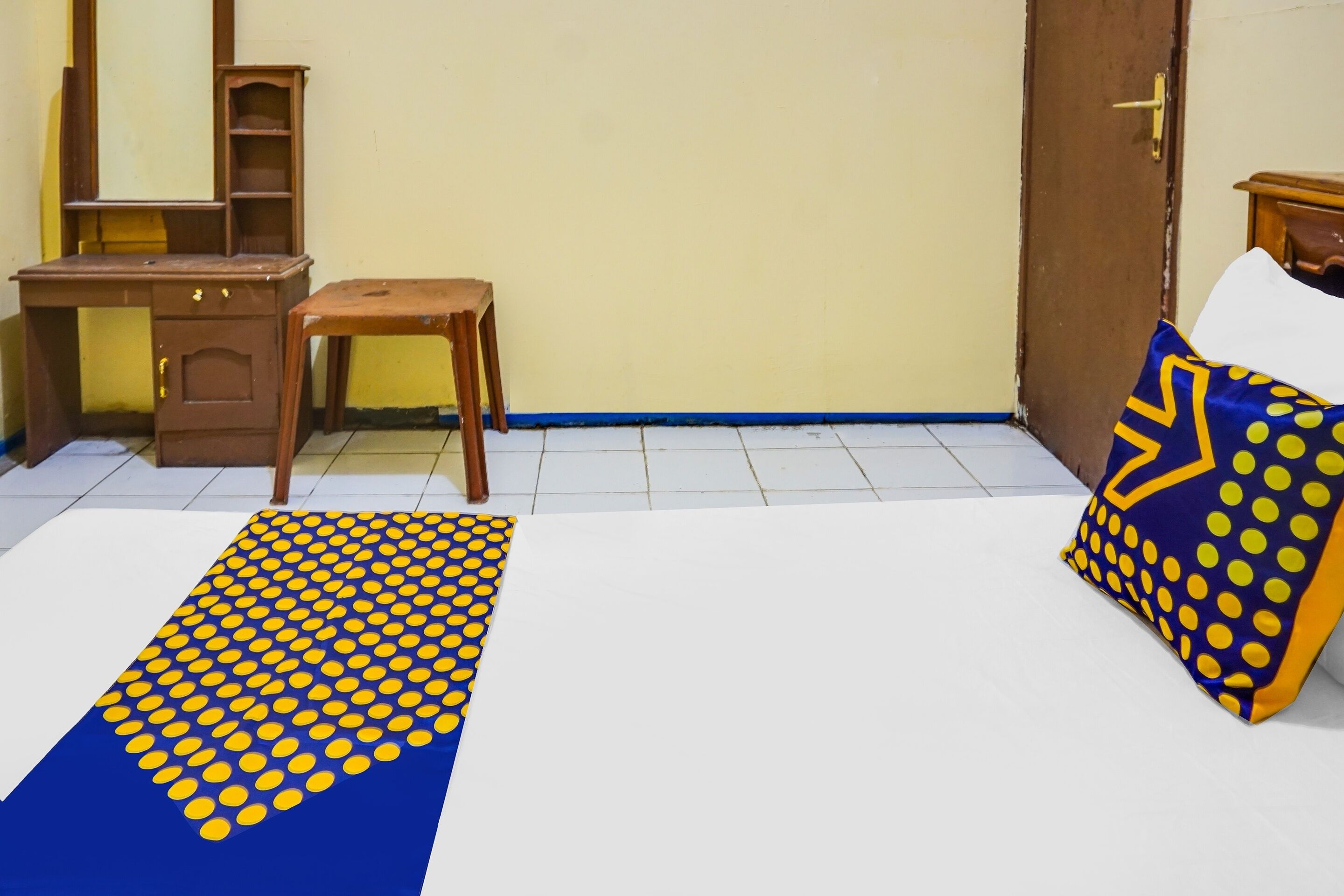 Une pièce comprenant un bureau, une chaise et un lit agrémenté d’un coussin à motifs.