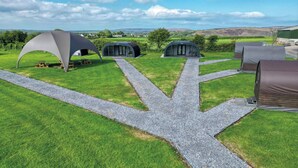 A campsite with multiple dome-shaped tents arranged in a semi-circle, connected by gravel paths. - Ocean View 1 - 1 Bed Pod - Llanrhidian (Swansea)