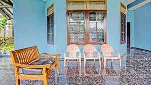 Una habitación con un banco de madera y tres sillas de plástico frente a una ventana con vidrieras decorativas.