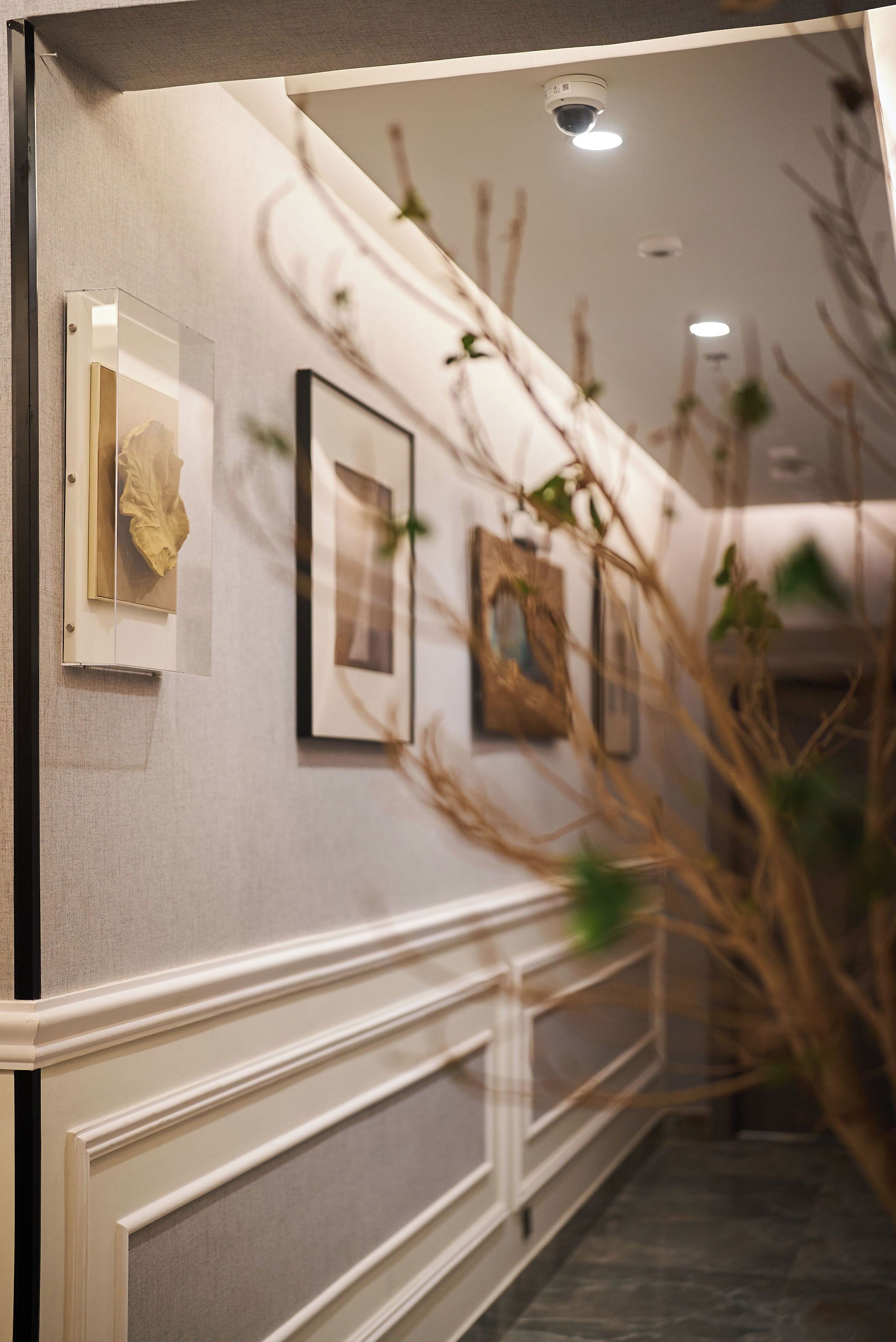 Un couloir orné de tableaux encadrés, avec une rambarde blanche et une caméra de surveillance fixée au plafond.