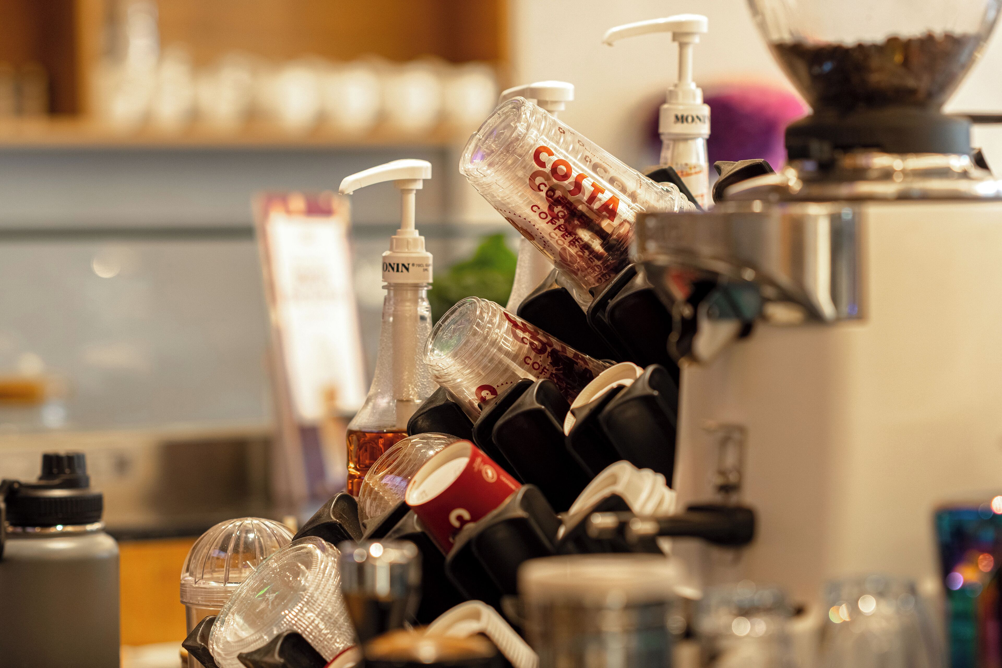Una cafetera con varias tazas y una botella de Costa Coffee.