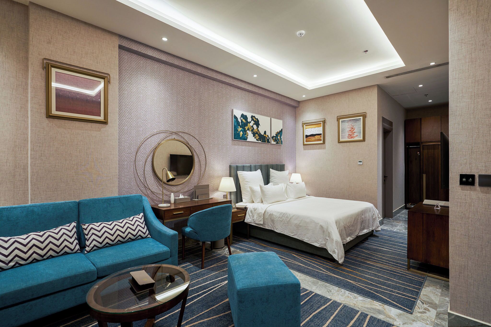 A hotel room with a bed, a sofa, a desk, a chair, and a small table.