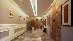 Pasillo de hotel con suelo de mármol, obras de arte colgadas en la pared y una puerta de madera.