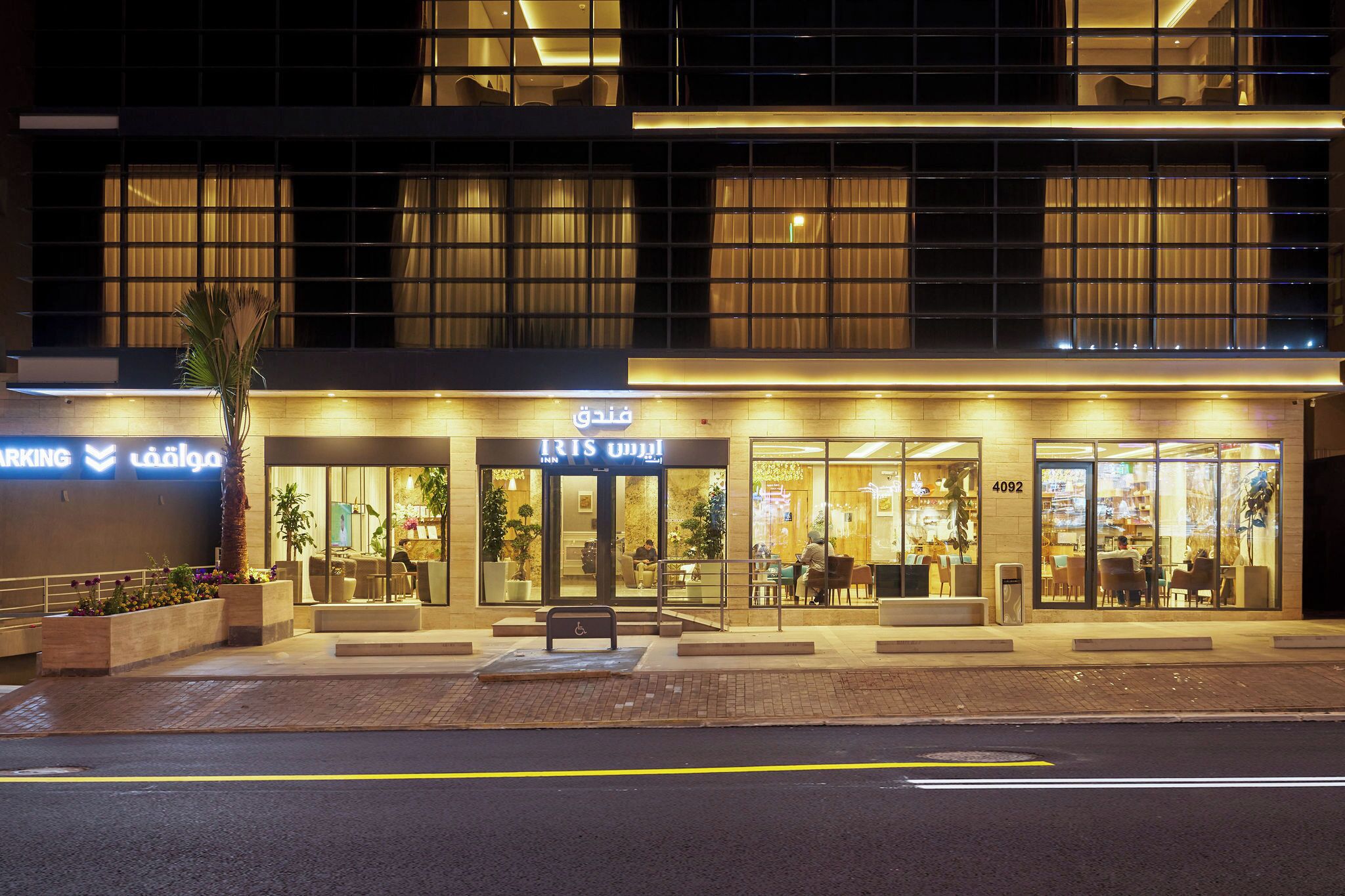 Un hotel moderno con una entrada bien iluminada, un área de estar al aire libre y un letrero de estacionamiento visible.