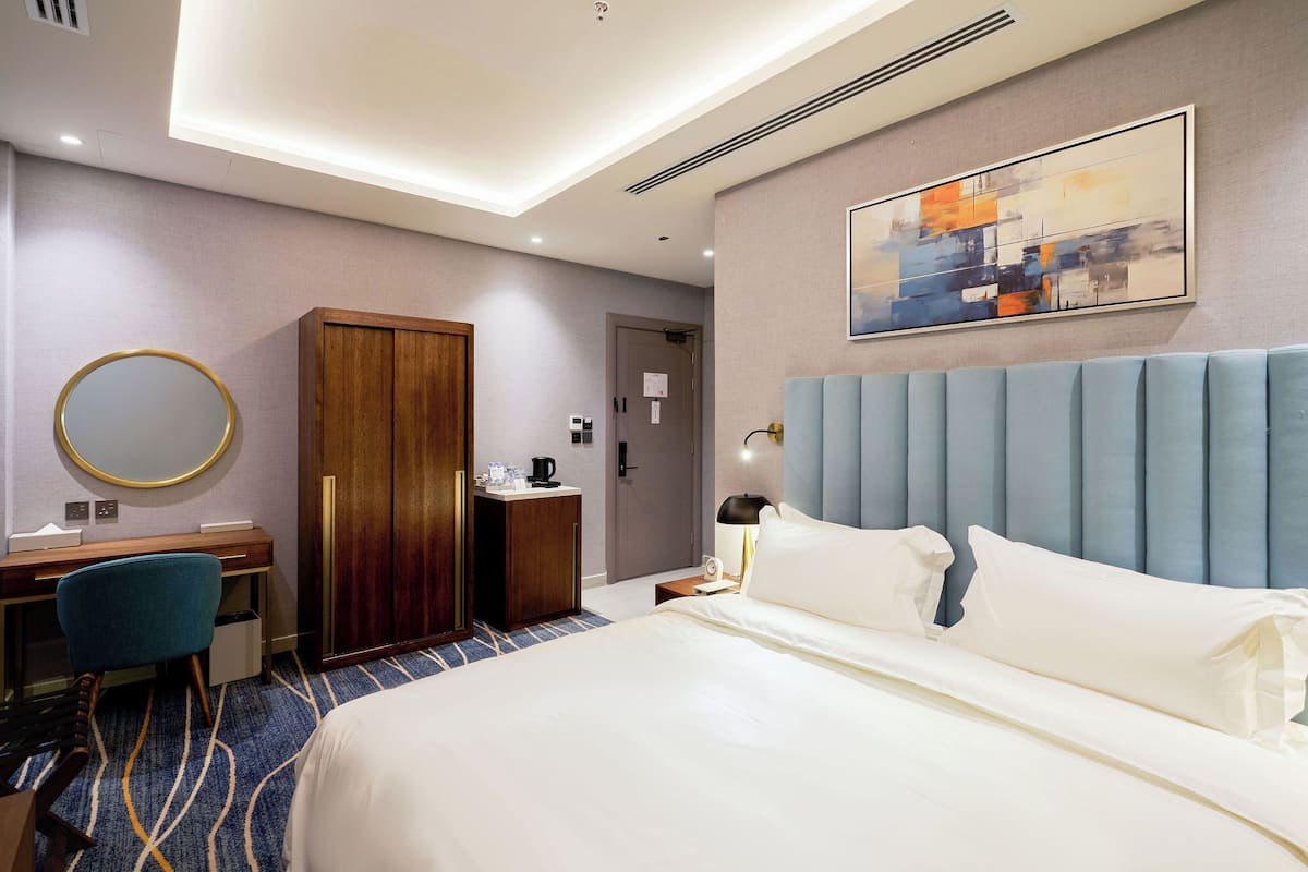 A hotel room with a bed, a desk, a chair, a wardrobe, and a bathroom door.