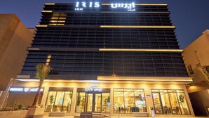 Un hotel moderno con un cartel llamativo de IRIS INN, que presenta fachada de vidrio y señalización iluminada.