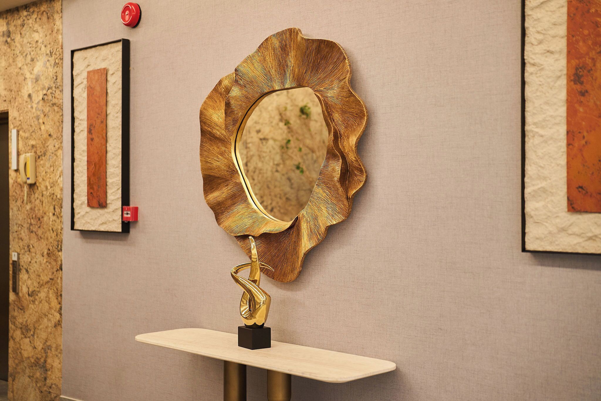 A wall-mounted mirror with a gold frame and a gold base, set on a light-colored console table.